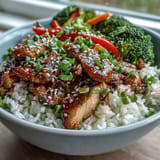 Golden chicken pieces coated in sticky honey garlic sauce rest on steamed rice with colorful bell pepper strips.