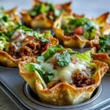 Appetizer mini taco cups with vibrant toppings piled high on wonton wrappers.