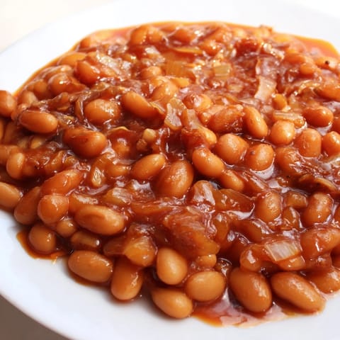 A spoon lifts tender beans from a sweet and smoky pot of homemade Baked Beans, perfect for cookouts.