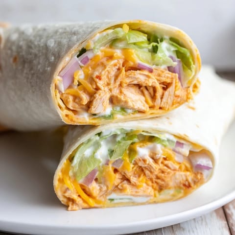 Warm, golden-brown Buffalo Ranch Chicken Wraps resting on a wooden cutting board, drizzled with extra ranch dressing and a hint of spicy buffalo sauce.