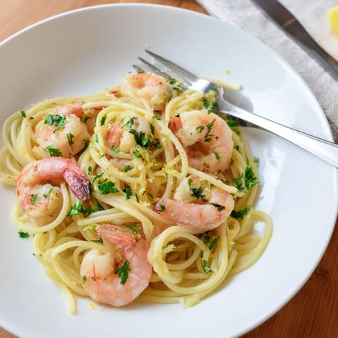 A close-up of plump, pink shrimp nestled in strands of pasta, glistening with a zesty garlic and lemon sauce, ready to serve.  