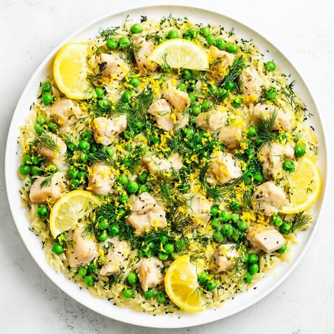 A vibrant skillet of Lemon Herb Chicken Orzo with tender chicken pieces, bright green peas, and fresh parsley garnish.