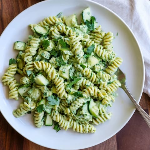 A close-up of the chilled vegetarian Green Goddess Pasta Salad highlights tender pasta, diced cucumbers, and vibrant parsley and chives tossed in a luscious, herb-packed dressing.  