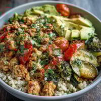 Seasoned ground turkey with roasted red bell peppers and zucchini on a bed of brown rice in a ceramic bowl with a lime wedge and fresh cilantro garnish.