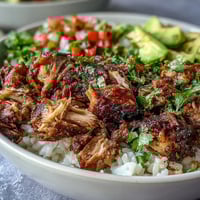 Shredded, crispy carnitas topped with creamy avocado and fresh pico de gallo in this vibrant bowl.