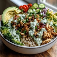 Freshly steamed broccoli and creamy avocado top this vibrant Rotisserie Chicken Bowl with hearty brown rice and juicy shredded chicken, drizzled with tzatziki sauce.