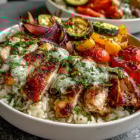 Golden-brown Lemon Herb Roasted Chicken Breast sliced over fluffy white rice and colorful roasted vegetables in a white bowl.